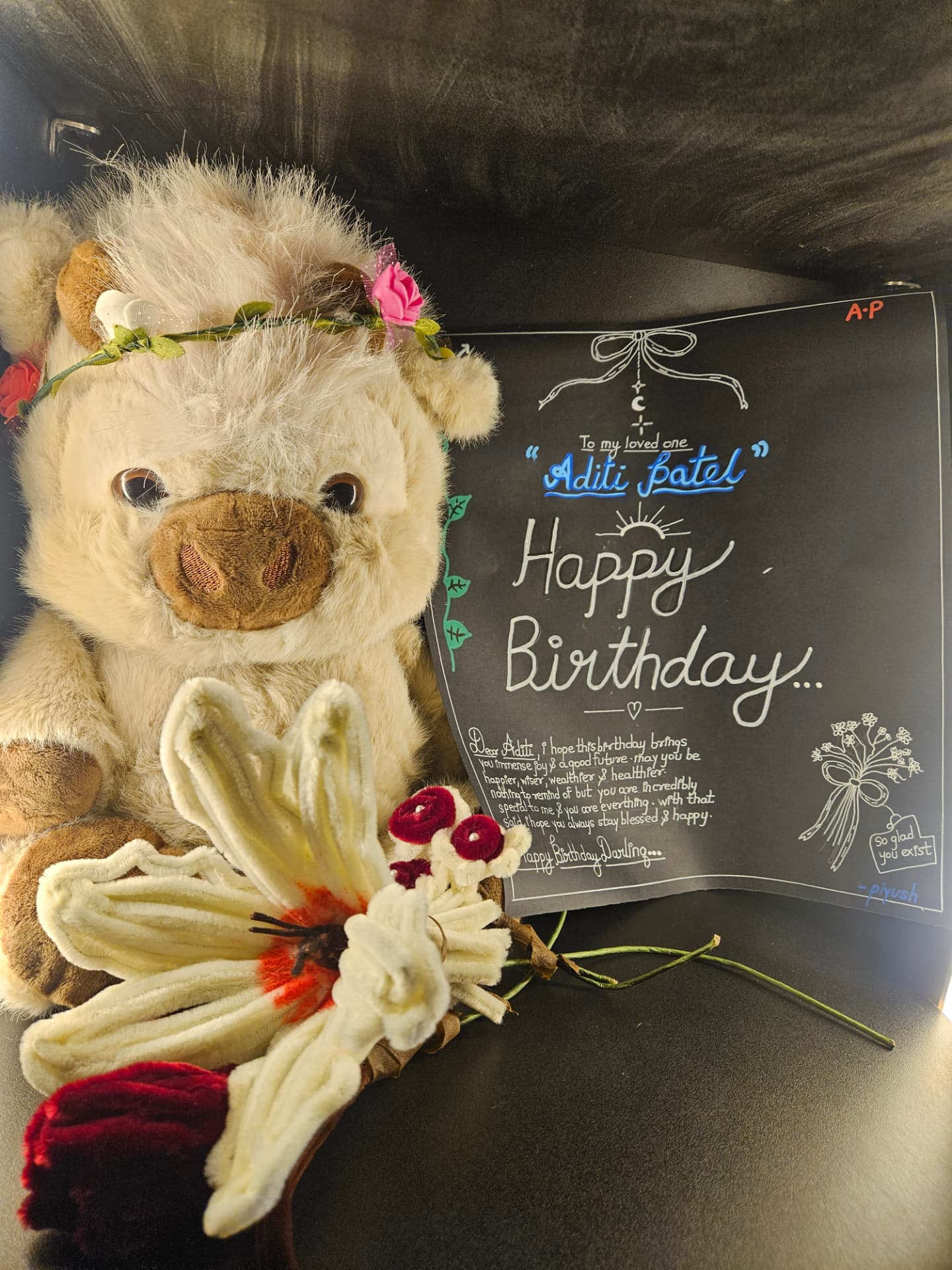 teddy bear with handmade flowers beside a handwritten happy birthday card for aditi