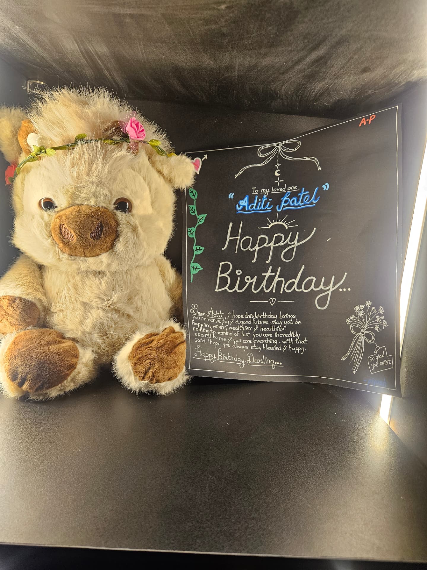 plush teddy bear wearing a flower crown beside a handwritten birthday card