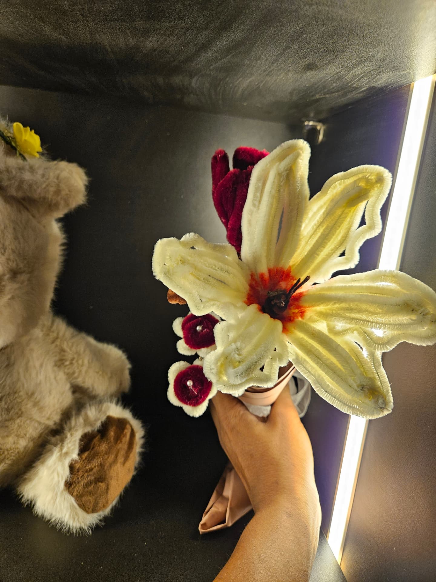 hand holding a bouquet of handmade cream and burgundy flowers beside a teddy bear